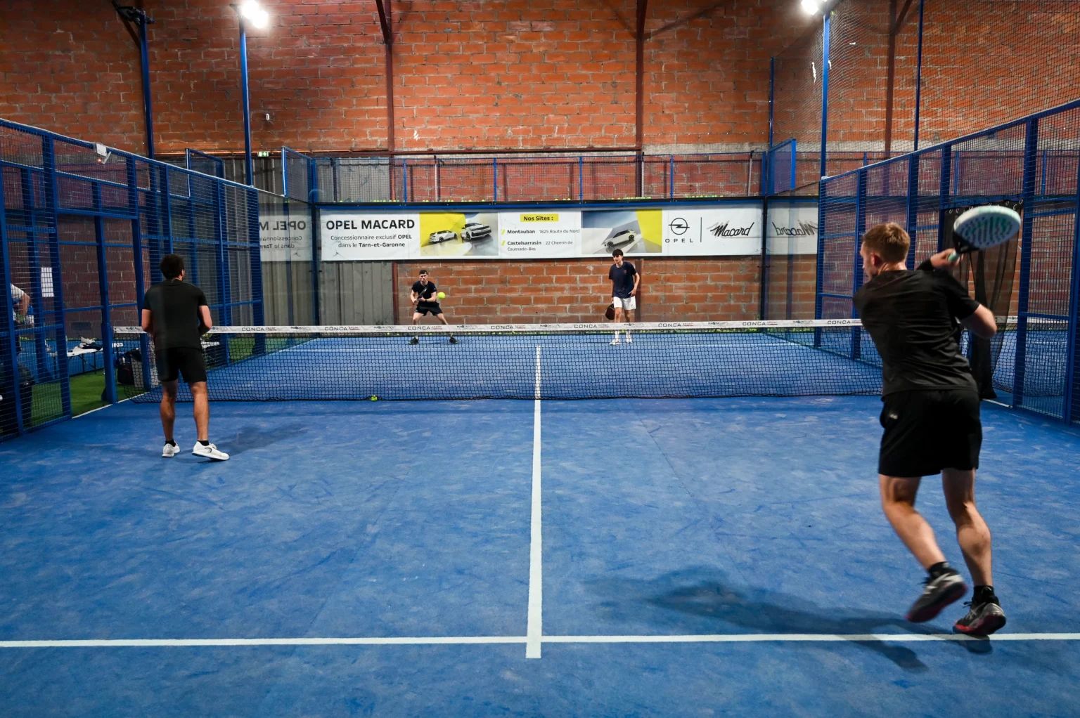 Terrains couverts du complexe Arena Montauban, joueurs en double sous la charpente
