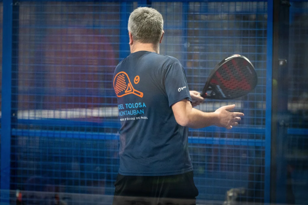 Joueur de padel de dos, maillot du club, au moment de la frappe