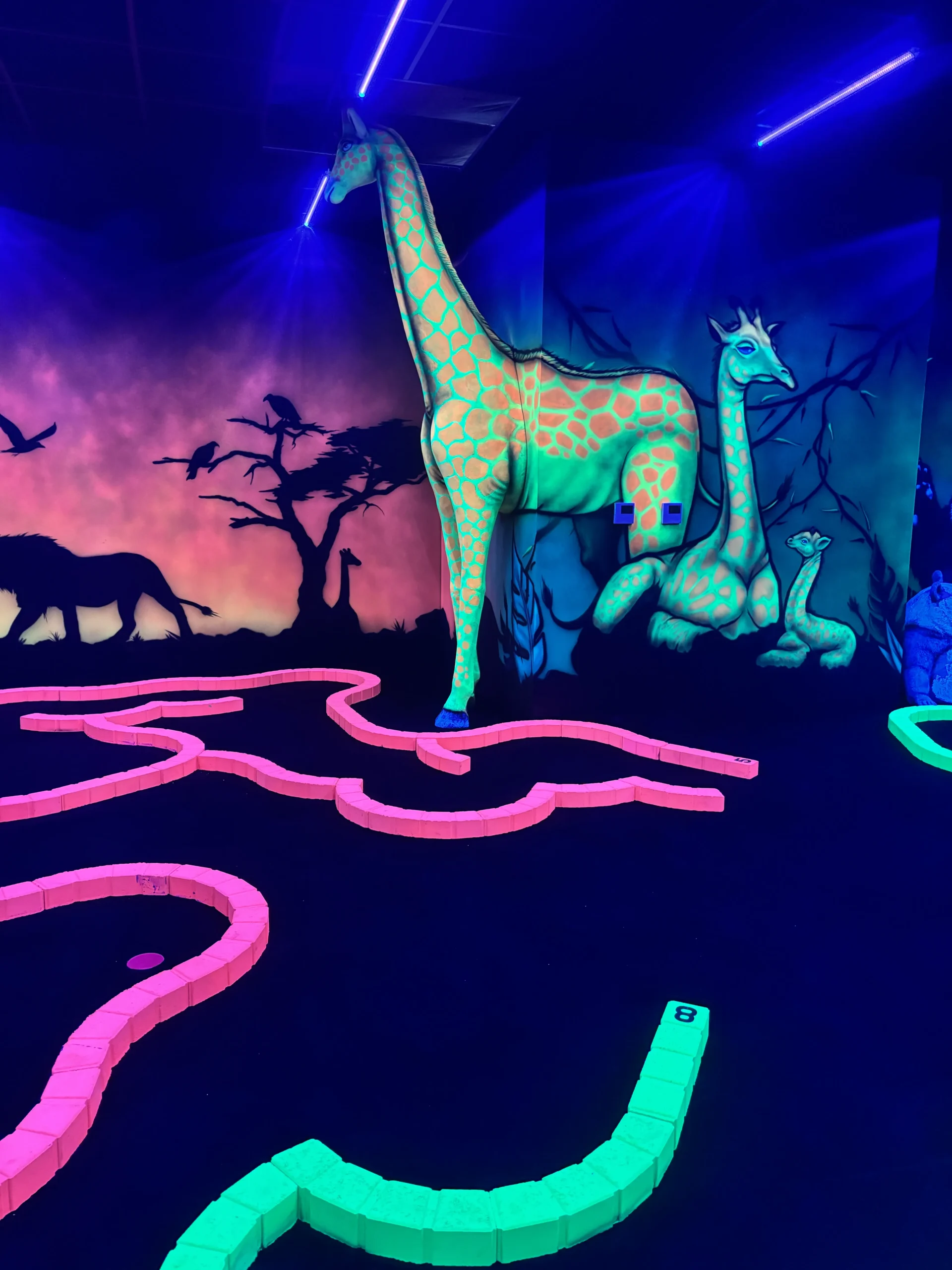 Girafe fluorescente et décor de savane sur un trou du parcours indoor