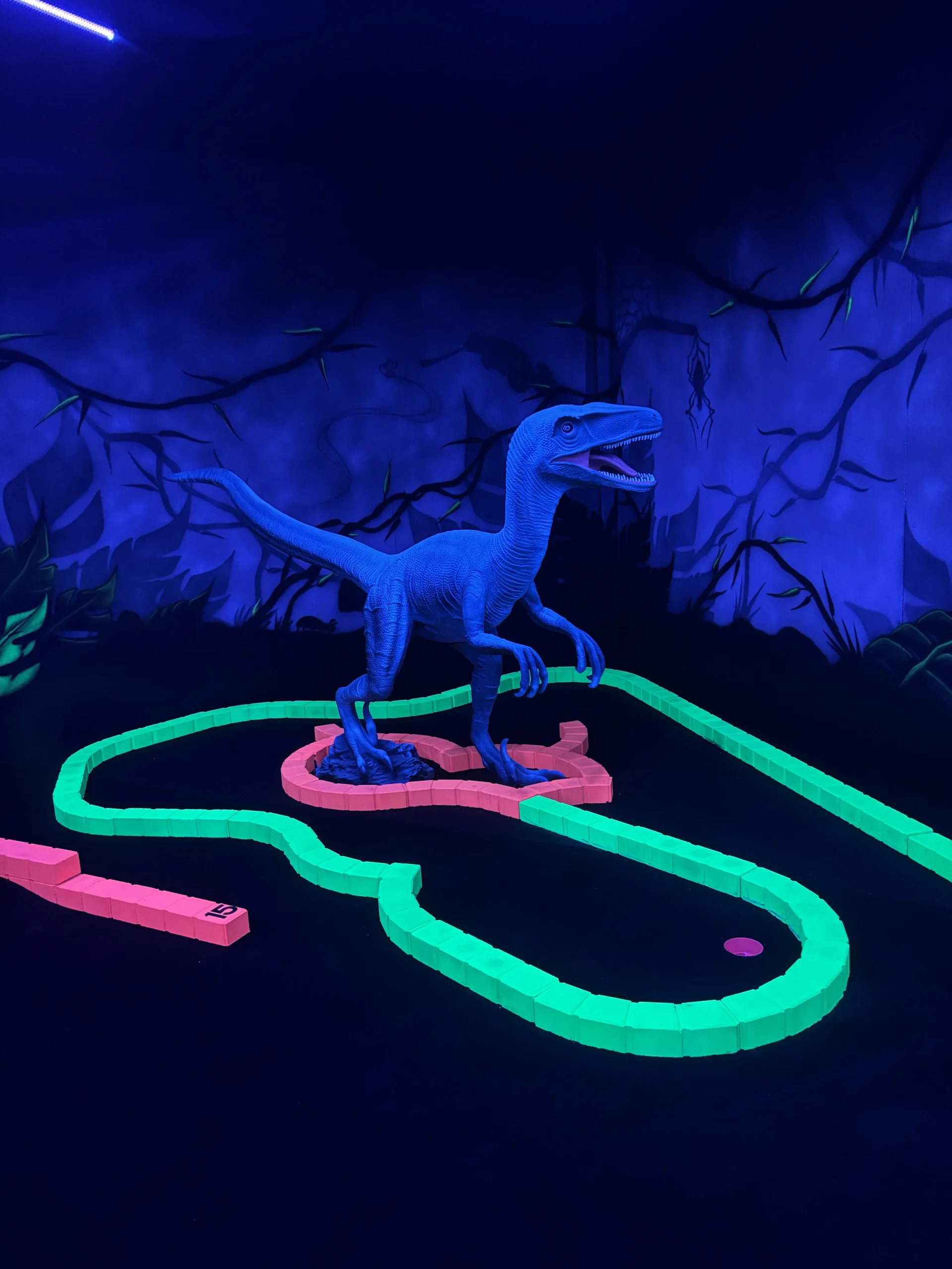 Dinosaure peint en bleu fluorescent posé au bord d’un trou du parcours