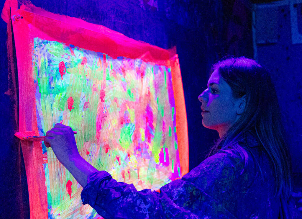Une participante peint une grande toile fluorescente au pinceau sous ultraviolets