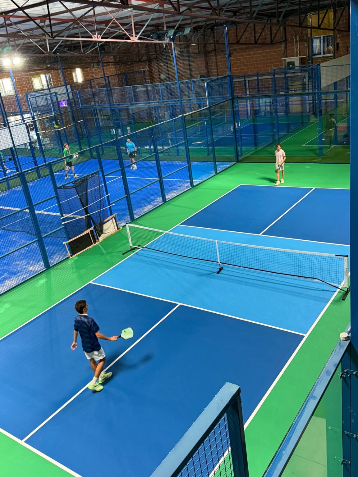 Partie de pickleball en double sur un terrain couvert de l’Arena Montauban, pistes de padel en fond